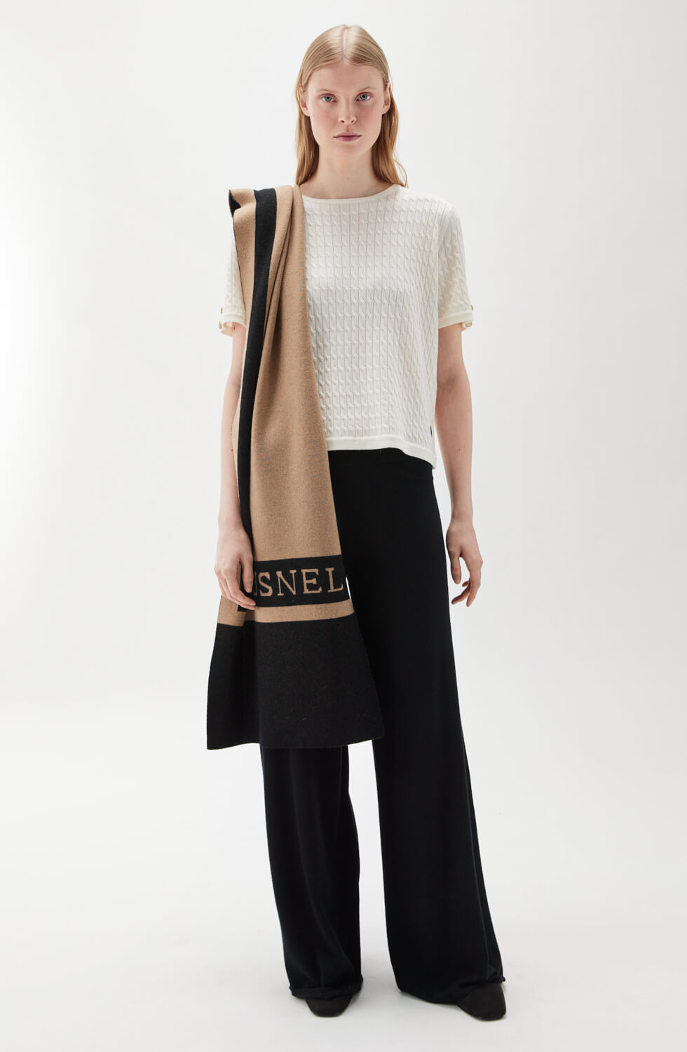 Woman wearing a white top and black pants with a beige scarf on a white background